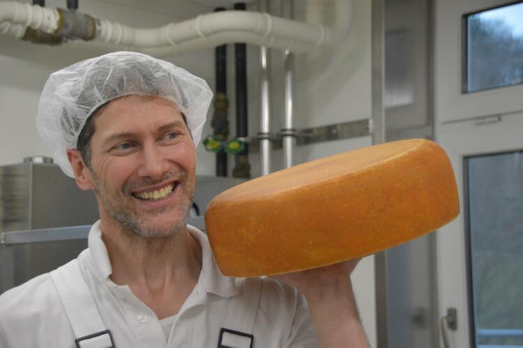 Rüdiger Spiegel Betriebsleiter auf dem Talhof stemmt mit einer Hand einen Laib Käse