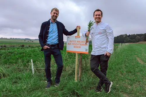 Dr. Christoph Reiber und Simon Tress auf dem Acker vor dem Schild: Gutes wächst auf fruchtbarem Boden.
