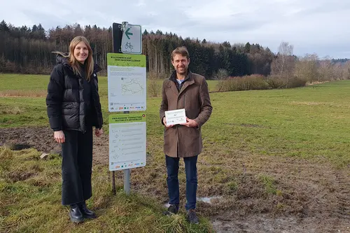 Laura Burkhardt und Dr. Christoph Reiber stehen neben einem Schild der Biohof-Genuss-Radtouren am Bodensee